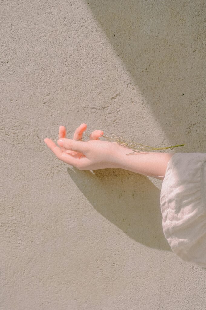A delicate hand extends towards a sunlit wall, capturing subtle textures and shadows.